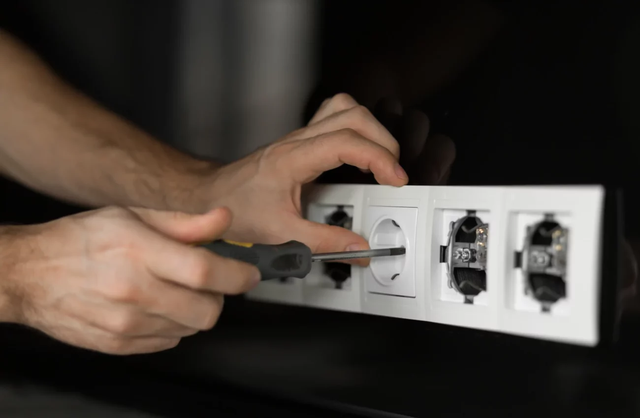 man-electrician-hand-with-screwdriver-disassembling-white-electrical-outlet-black-glass-wall-scaled-1.webp